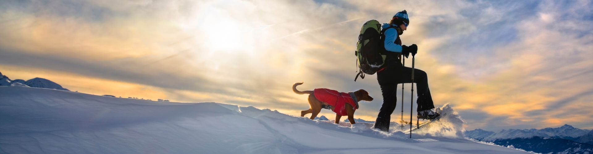 woman snowshoeing with her dog in a red jacket in the mountains