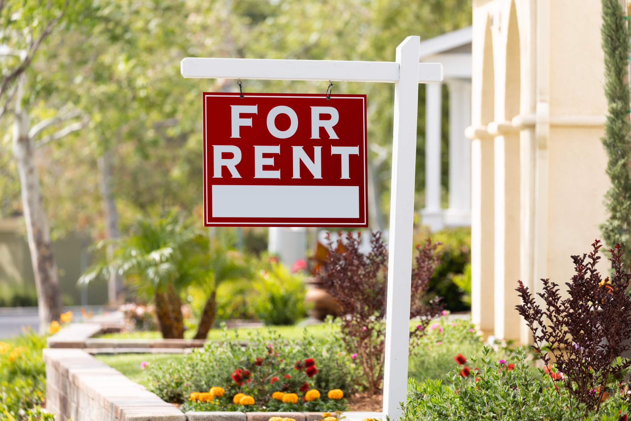 red "for rent" sign hanging on a white post outside of a house