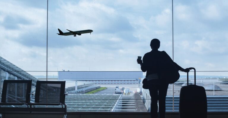 a person standing inside of an airport while a place takes off outside