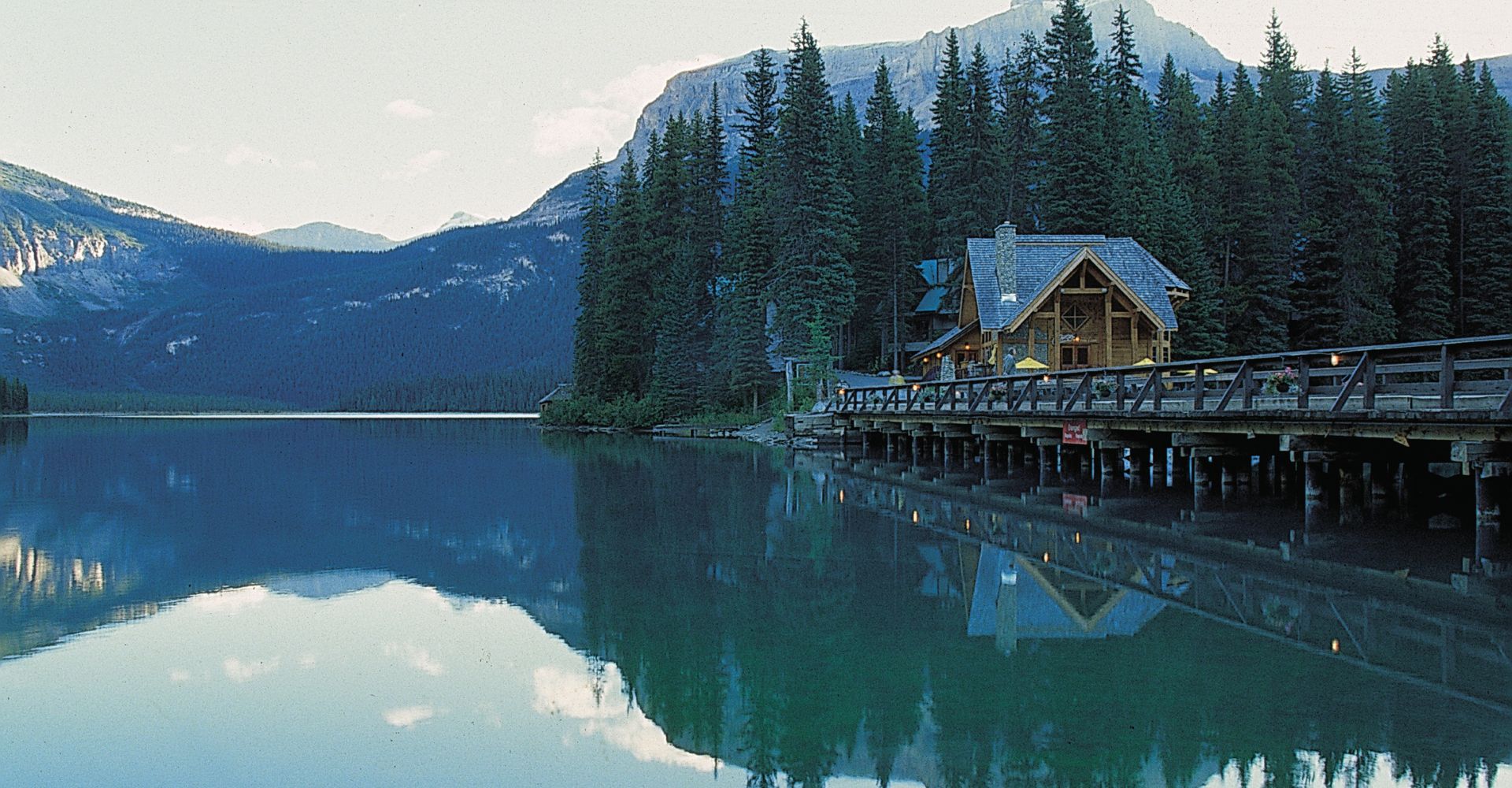 a lakeside cabin surrounded by evergreen trees with mountains in the background