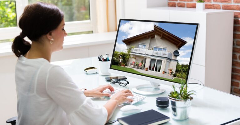 A woman sits at a desk, focused on a computer screen displaying an image of a house