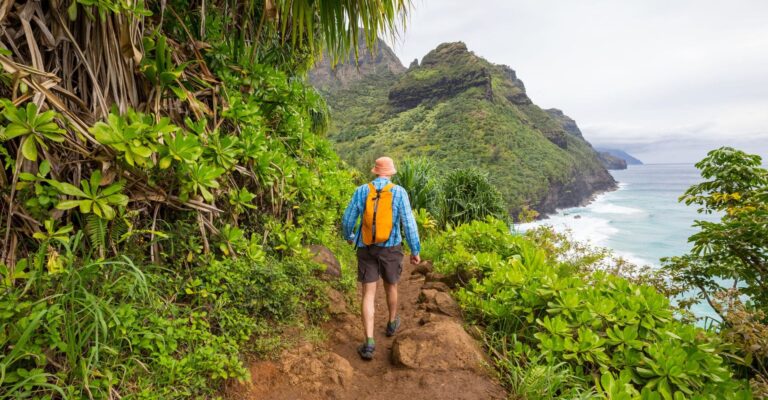 A man with a backpack hiking up a coastal trail, with the ocean visible in the background