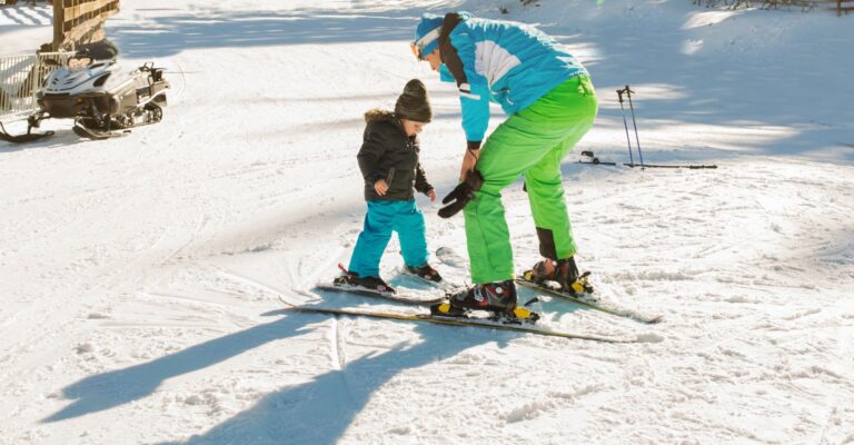 A woman assists a child on skis, both enjoying a day on the slopes surrounded by snow-covered trees