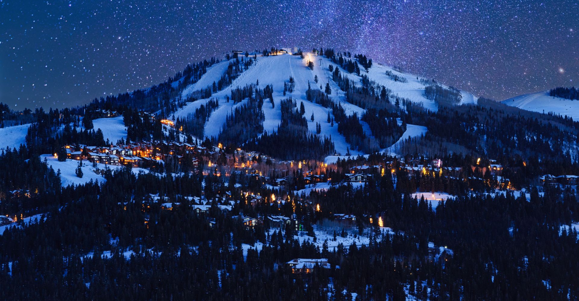 Snow-covered mountain at night, illuminated by bright lights on its peak, creating a serene winter landscape