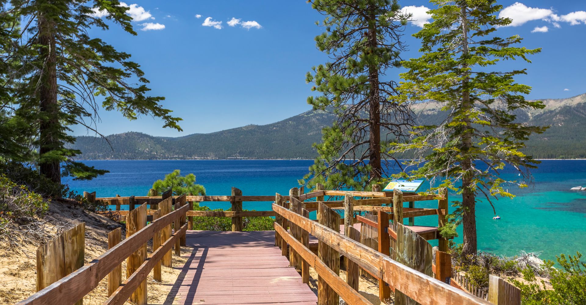 A wooden walkway extends towards a sandy beach and vibrant blue water under a clear sky