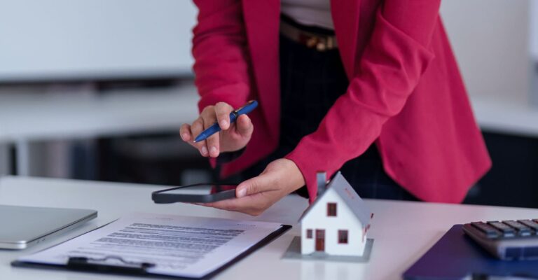 A woman is seated at a desk, using a pen to sign important documents, surrounded by office supplies