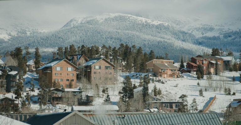 A snowy mountain range with scattered houses and evergreen trees in the foreground, showcasing a serene winter landscape