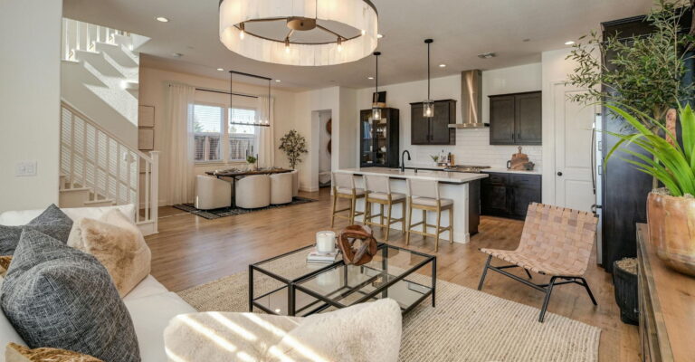 Modern open-concept living space featuring a kitchen with dark cabinets, island seating, dining area, and neutral-toned furnishings with natural light.
