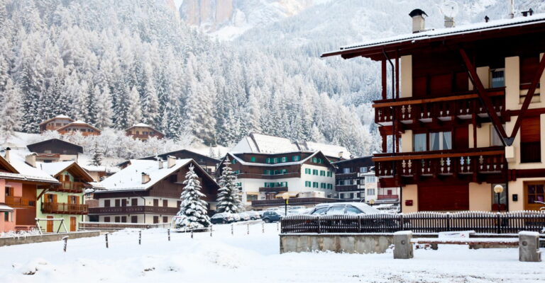 Snow-covered village with wooden chalets and evergreen trees in a mountainous landscape during winter.