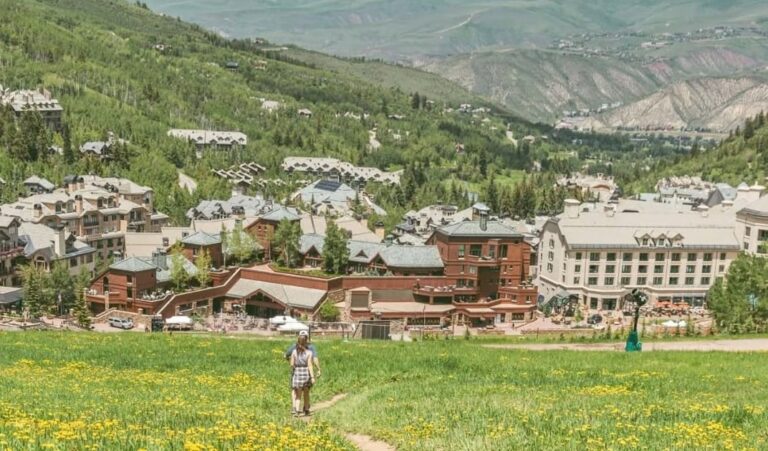 Two people stroll along a scenic mountain path in front of a beautiful resort, surrounded by lush greenery.